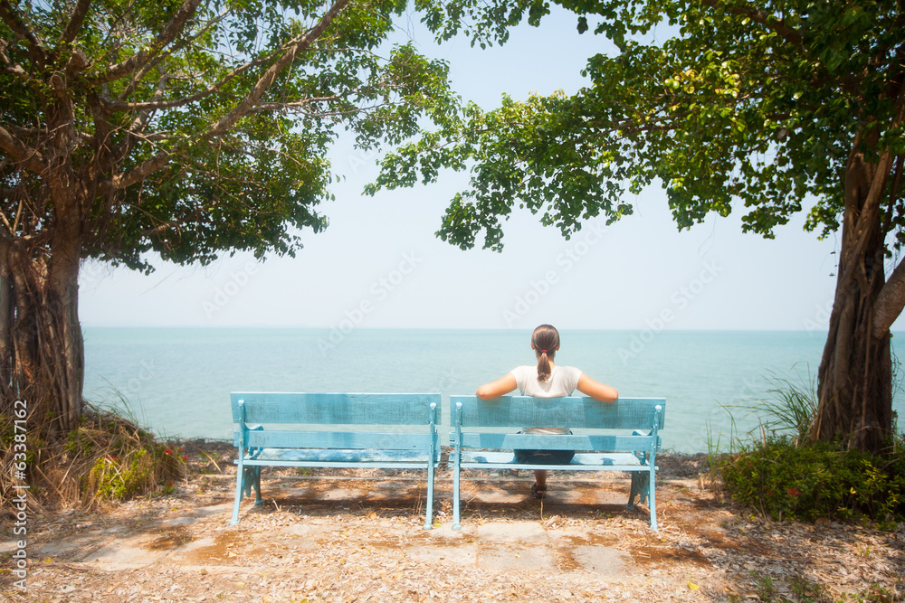 Young woman sitting on bench facing the sea