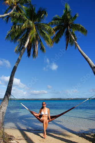 Young woman in bikini sitting in a hammock between palm trees, O photo