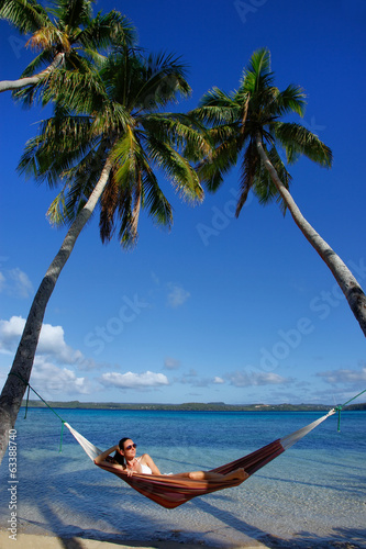 Young woman in bikini laying in a hammock between palm trees, Of photo