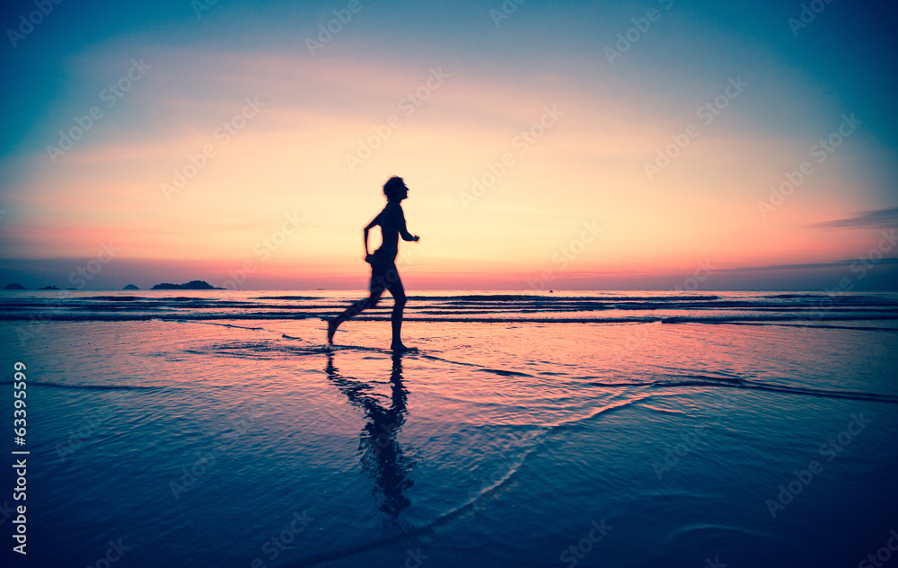 Blured silhouette of a woman jogger on the beach at sunset.