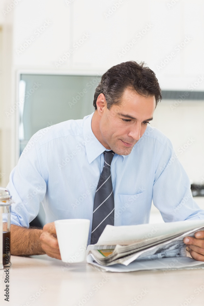Well dressed man with coffee cup reading newspaper in kitchen Well dressed man with coffee cup reading newspaper in kitchen