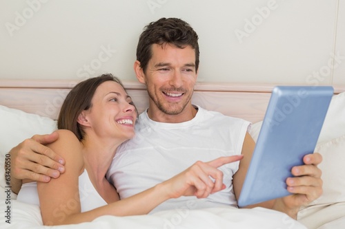 Happy couple using digital tablet in bed