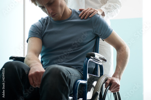 Doctor consoling young man sitting in wheelchair