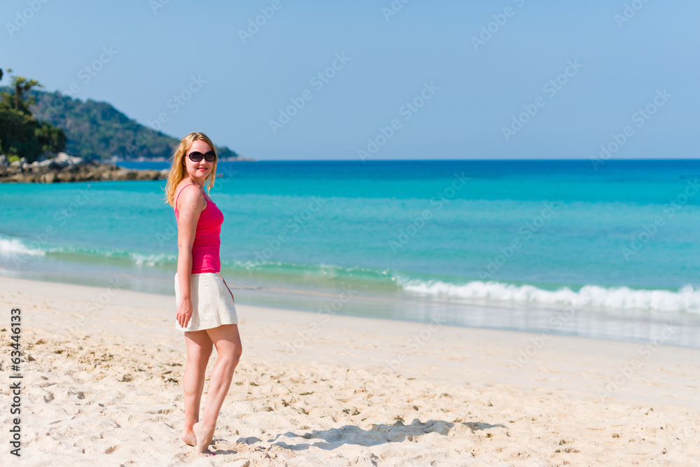 Young woman in pink top and beige skirt walking on beach