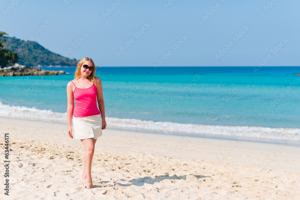 Young woman in pink top and beige skirt walking on beach