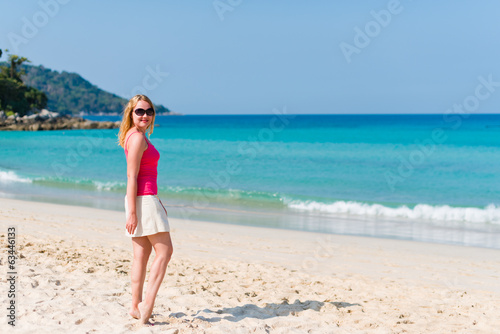 Young woman in pink top and beige skirt walking on beach