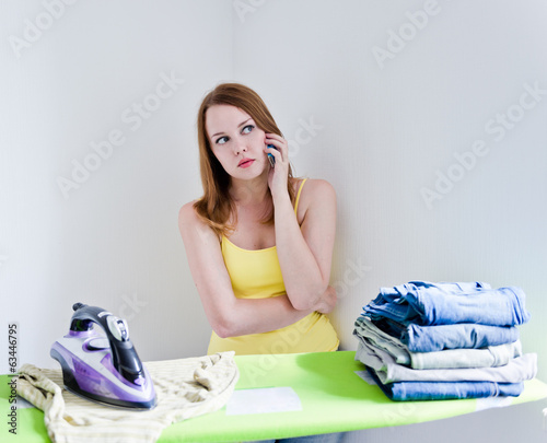 Housewife talking on the phone while ironing on grey background