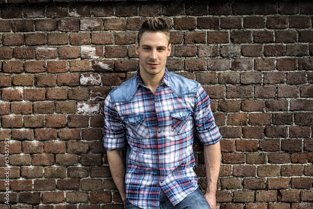 Smiling young man leaning on old brick wall Smiling young man leaning on old brick wall