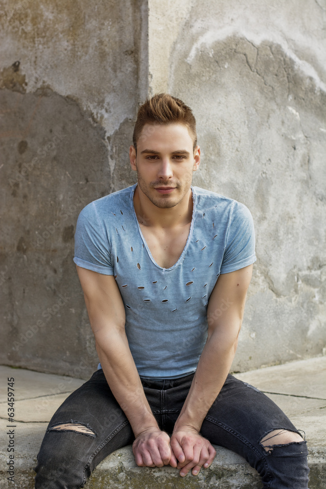 Fototapeta premium Smiling young man sitting on cement.