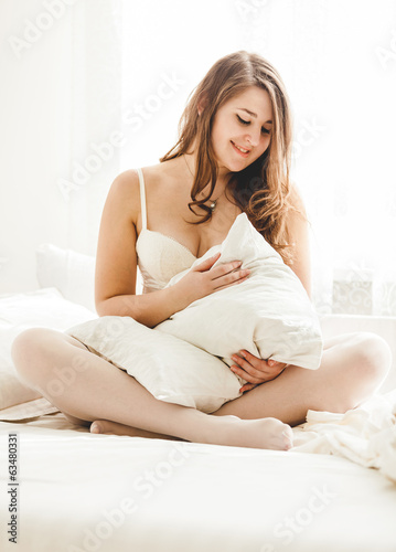 cute woman hugging pillow on bed