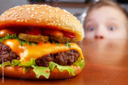 Hungry young boy is staring and smelling a burger photo