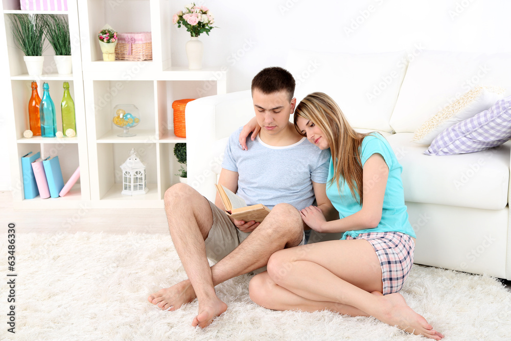 Beautiful couple reading book, sitting carpet sofa, home Beautiful couple reading book, sitting carpet sofa, home