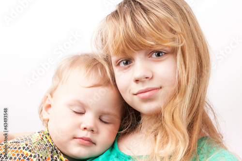 Little blond Caucasian girl with sleeping sister. Portrait on wh