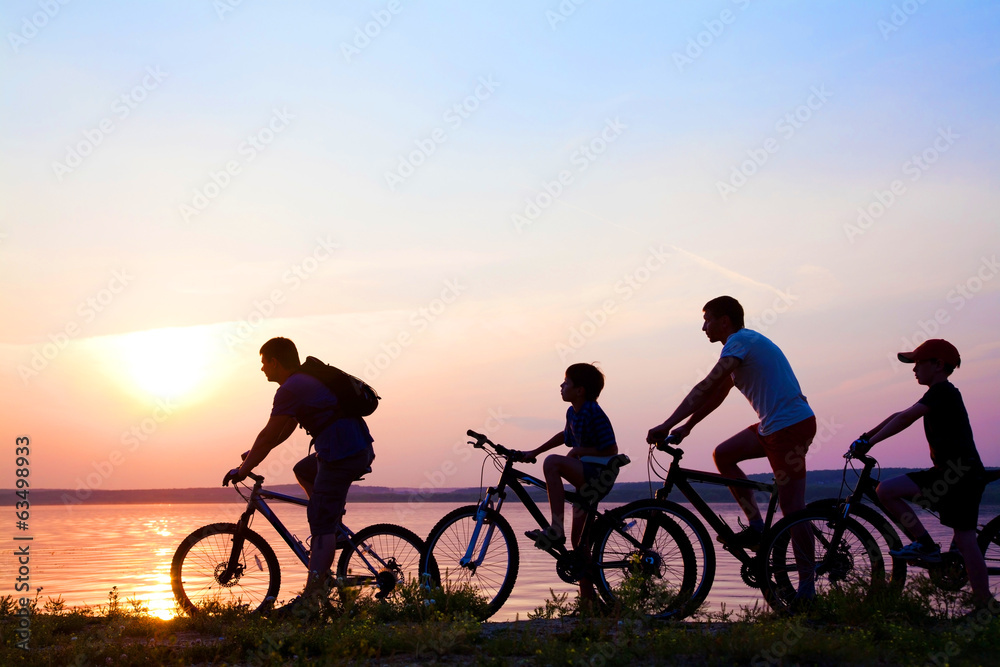family on bicycles admiring the sunset on the lake. silhouette