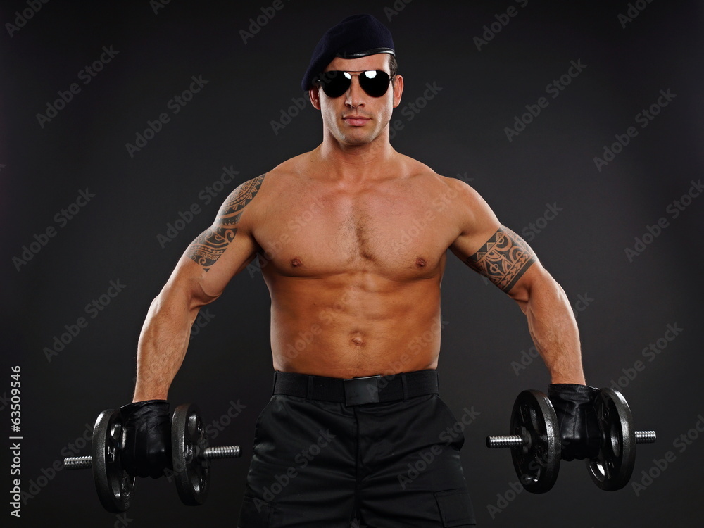Portrait of muscular soldier at sunglasses holding dumbbells