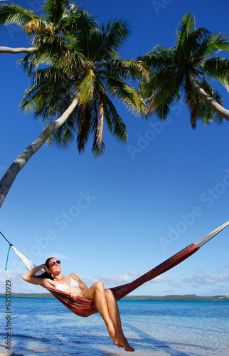 Young woman in bikini sitting in a hammock between palm trees, O photo