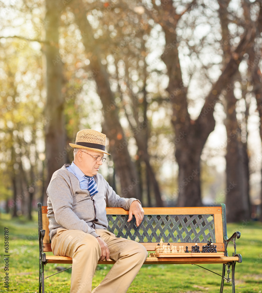Senior playing chess alone seated on bench in park Senior playing chess alone seated on bench in park