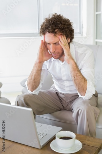 Worried man with head in hands looking at laptop at home