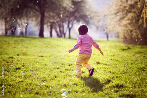 Little boy, running in the park, chasing soap bubbles