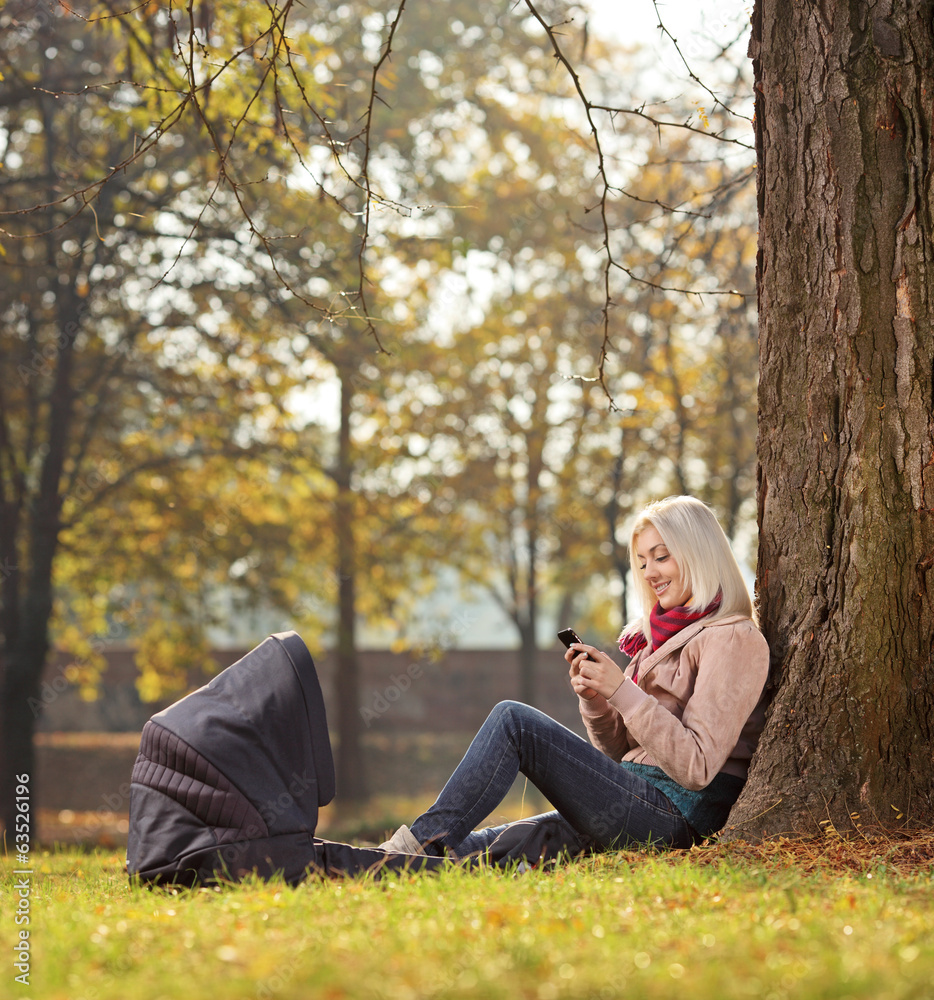 Obraz premium Blond girl texting by phone seated in park