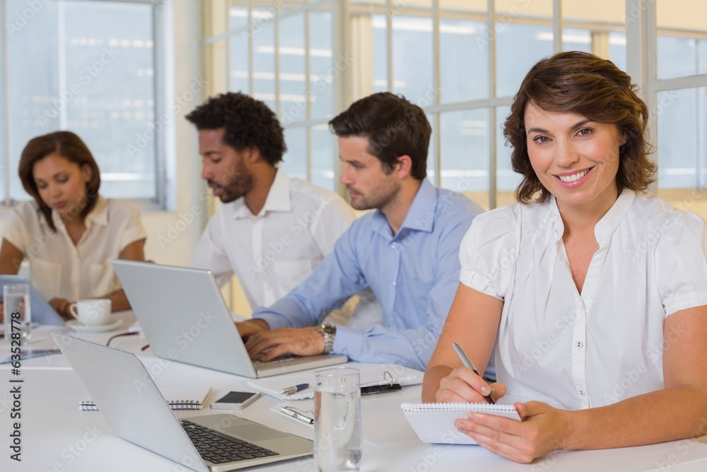 Smiling businesswoman writing notes with colleagues in meeting a