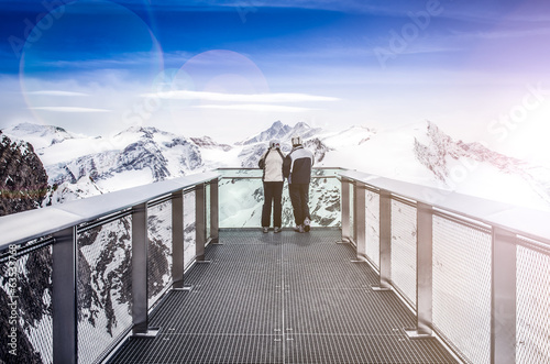 Two people looking at Alps mountains from viewpoint platform photo