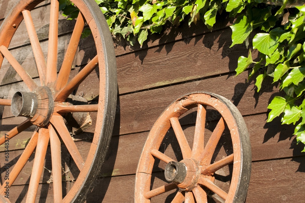 Old carriage wheels hanging on board wood wall