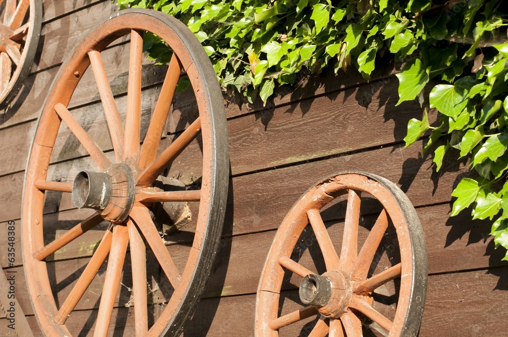 Fototapeta premium Old carriage wheels hanging on board wood wall