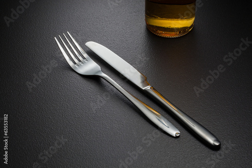 bottle of beer, knife and fork on black photo