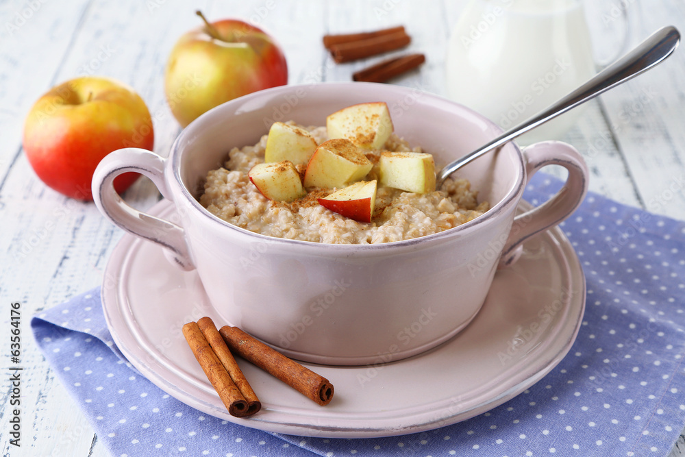 Tasty oatmeal with apples and cinnamon on wooden table Tasty oatmeal with apples and cinnamon on wooden table