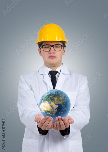 A man wearing a white robe and a yellow cap holding the Earth.