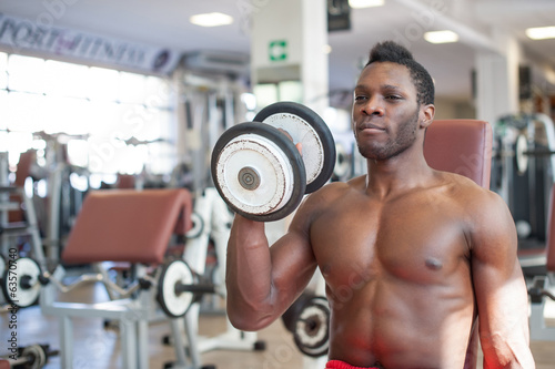 Strong black man exercising with dumbbells in the gym.