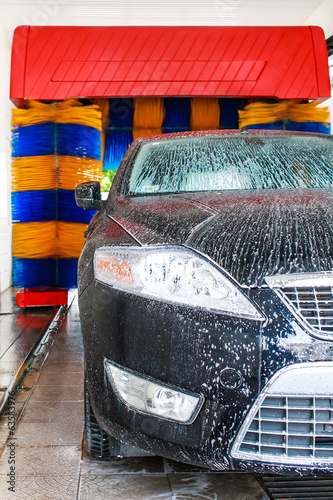 Black car in automatic car wash, rotating blue and yellow brushe