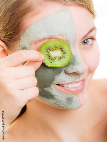 Woman in clay mask on face covering eye with kiwi photo