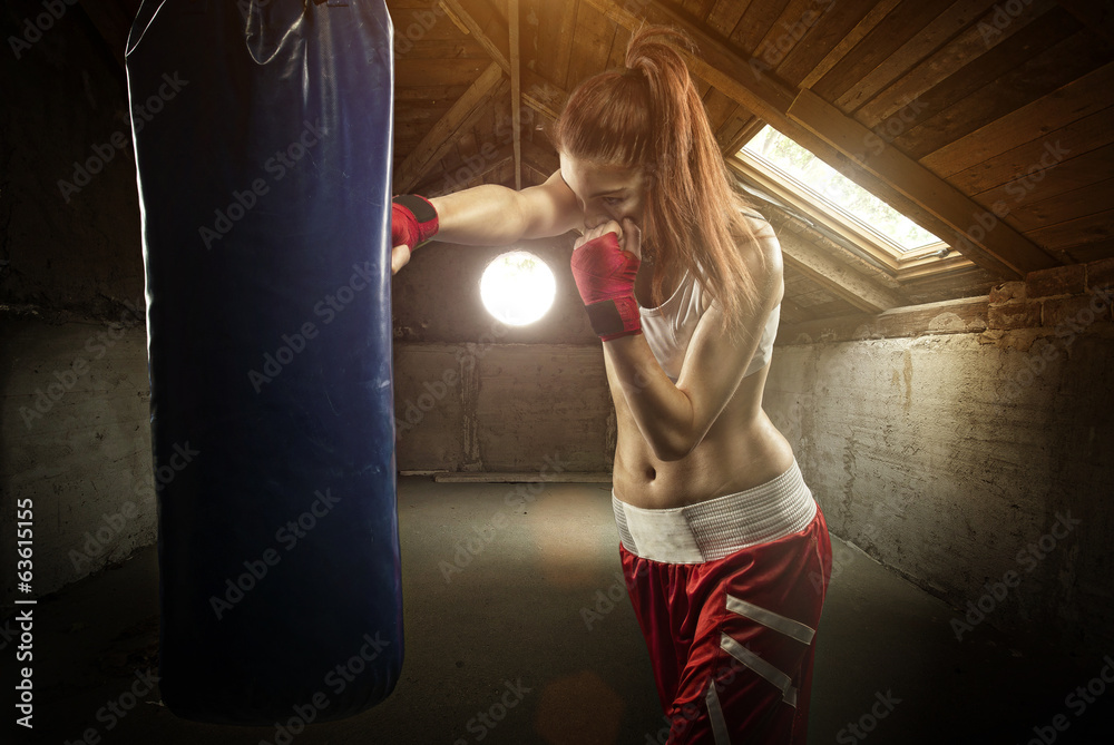 Young women boxing, hitting the boxing bag - on the attic