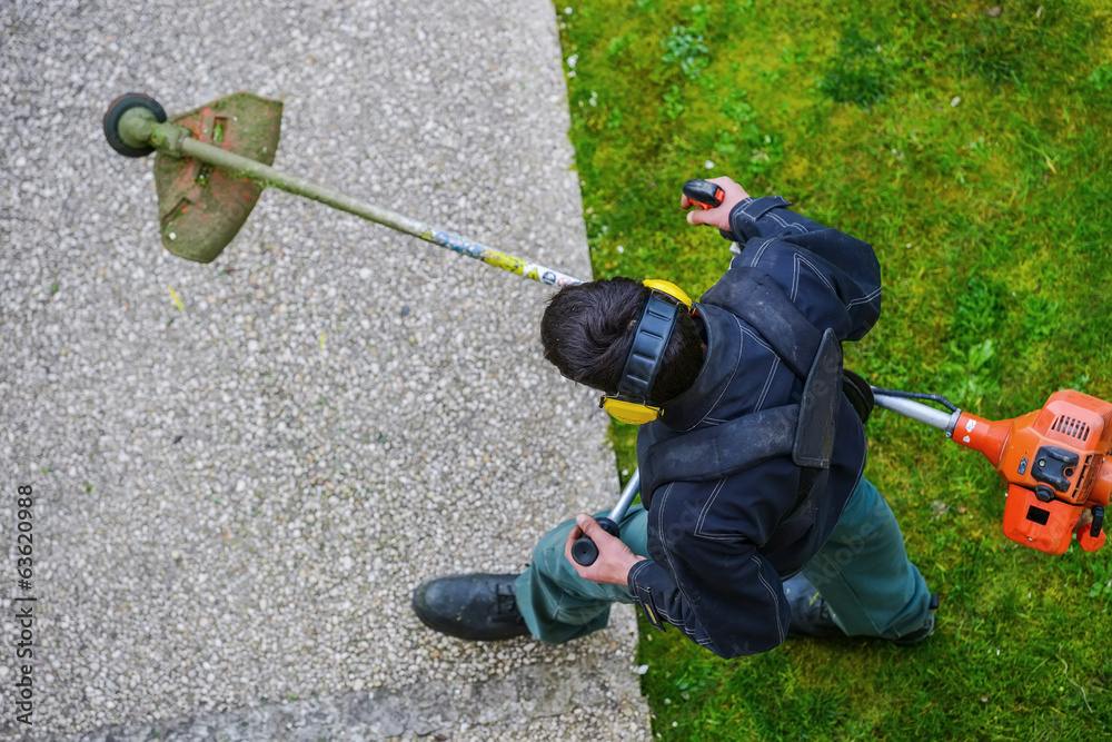 Obraz premium gardener using corded string trimmer in a park