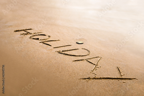 Holiday word written on the sand bright back light effect