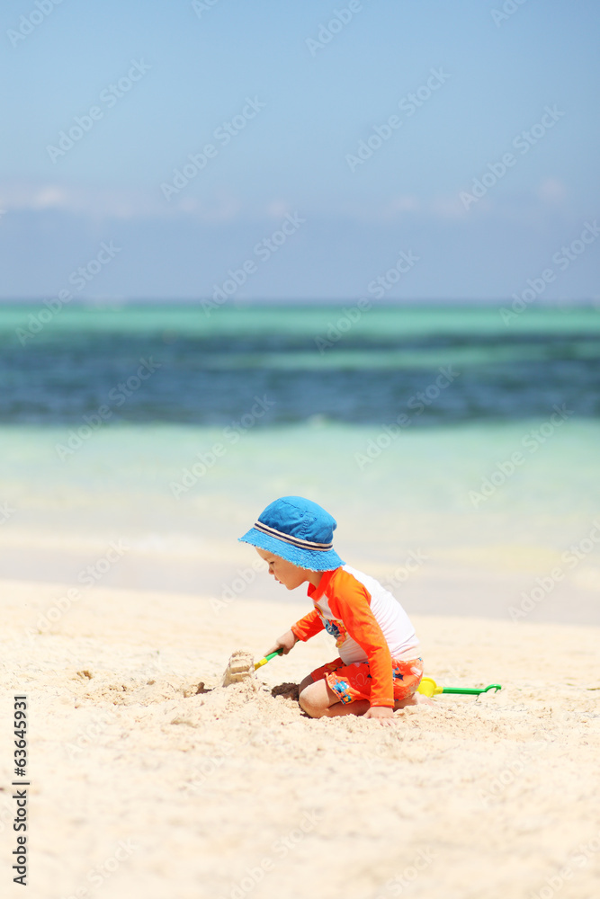 One caucasian boy playing with sand at tropical beach One caucasian boy playing with sand at tropical beach