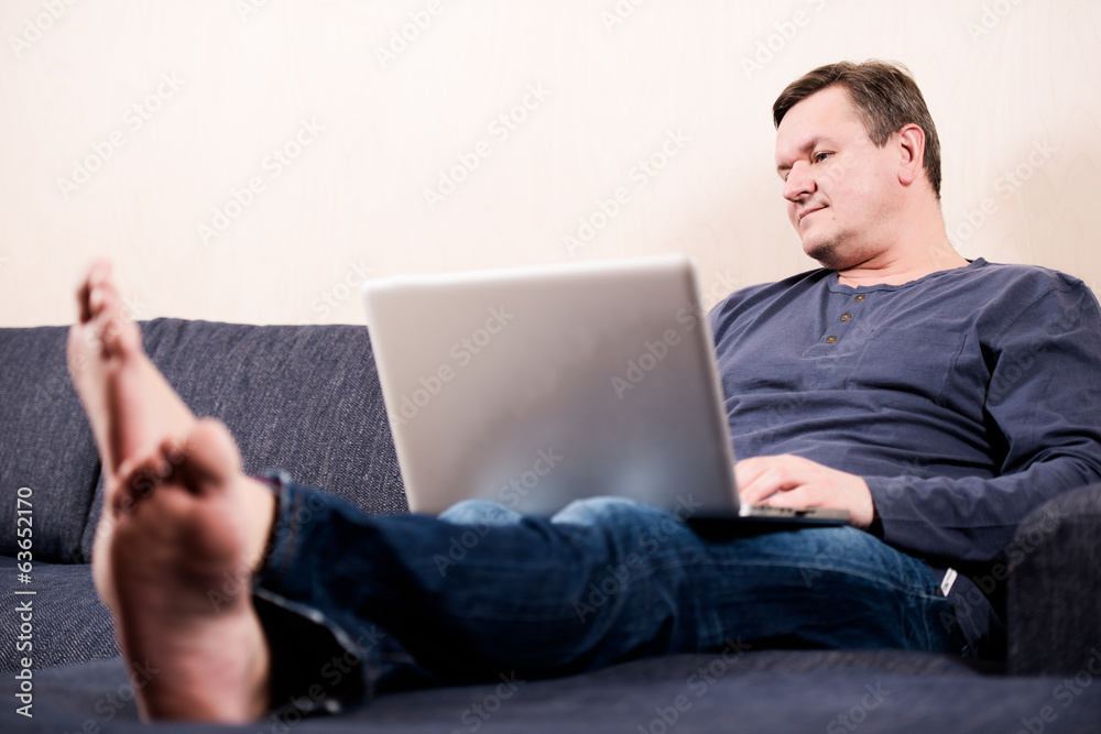 Man sitting on sofa with laptop barefoot