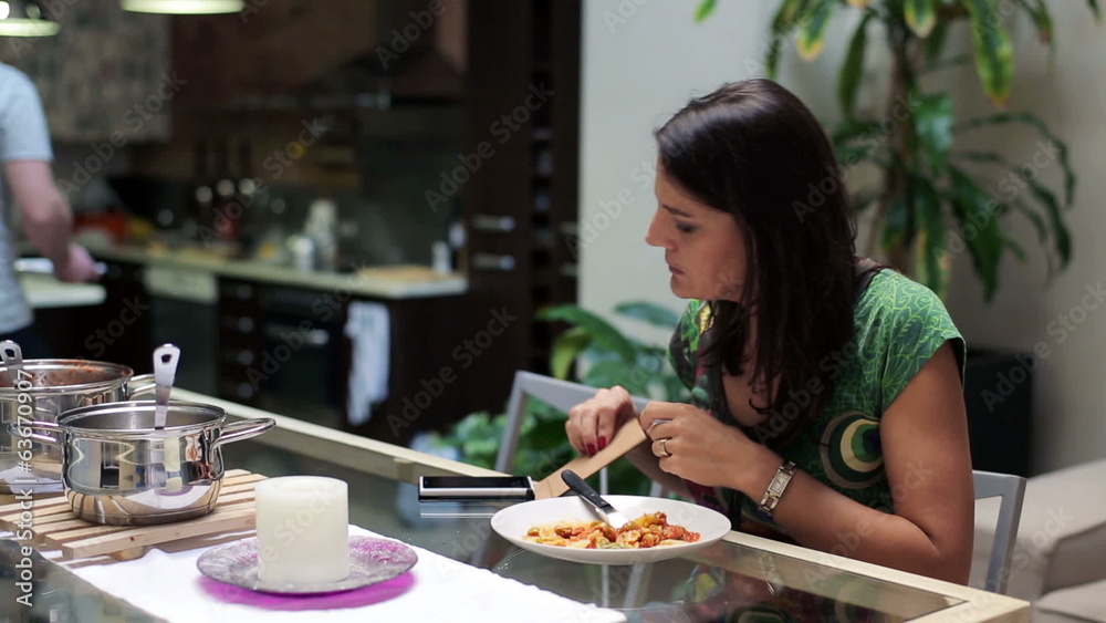 Woman eating dinner, using smartphone by the table at home Woman eating dinner, using smartphone by the table at home