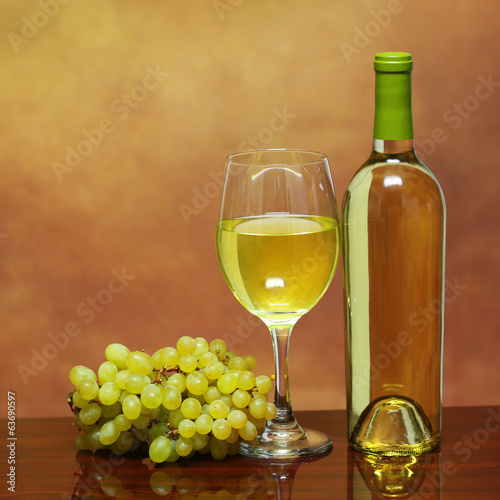 Wine Bottle and Glass of White Wine with Fresh Grapes over beige