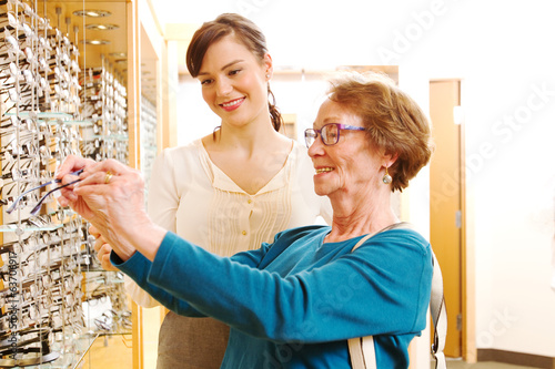 Fototapeta Naklejka Na Ścianę i Meble -  Optician assisting older lady with glasses
