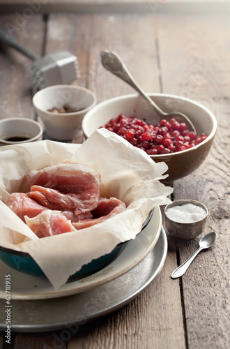 Raw pork in a bowl, cranberries, seasonings and meat hammer