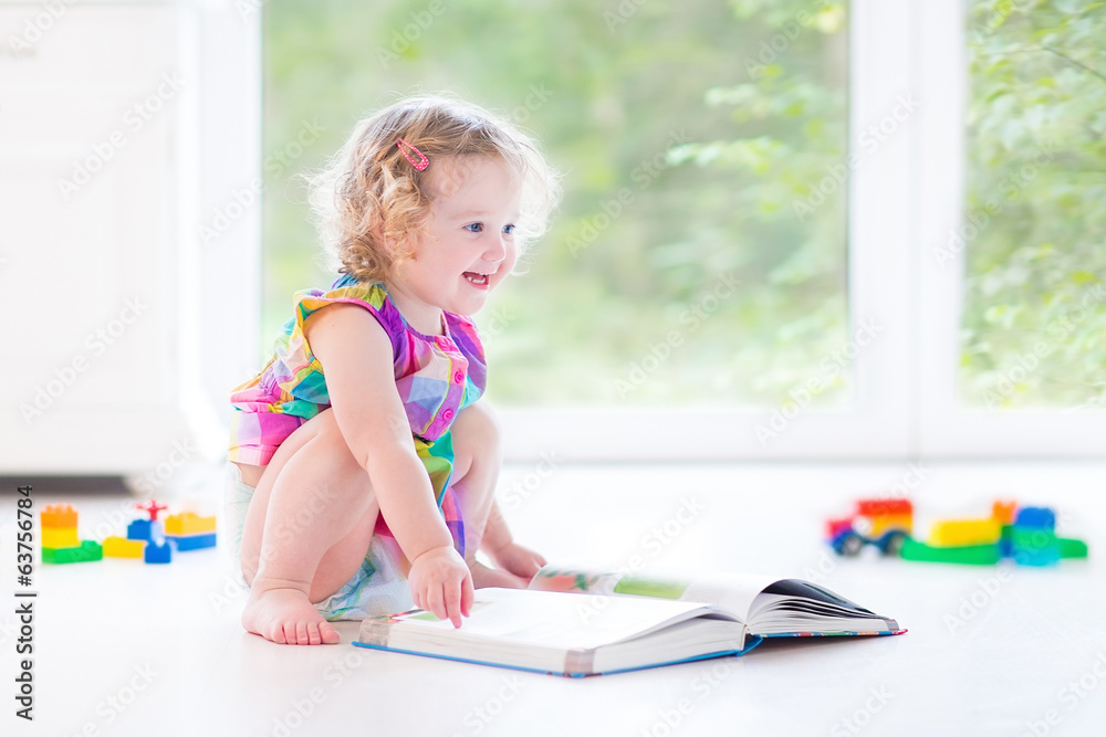 Cute toddler girl with blond curly hair reading a book Cute toddler girl with blond curly hair reading a book