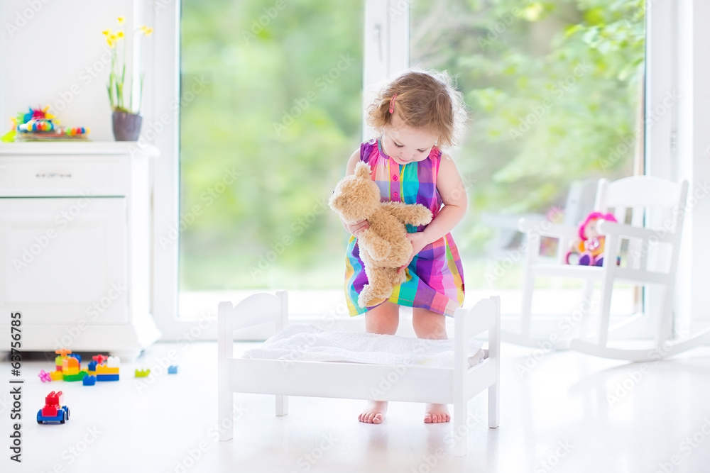 Adorable curly toddler girl in pink dress playing with her teddy Adorable curly toddler girl in pink dress playing with her teddy