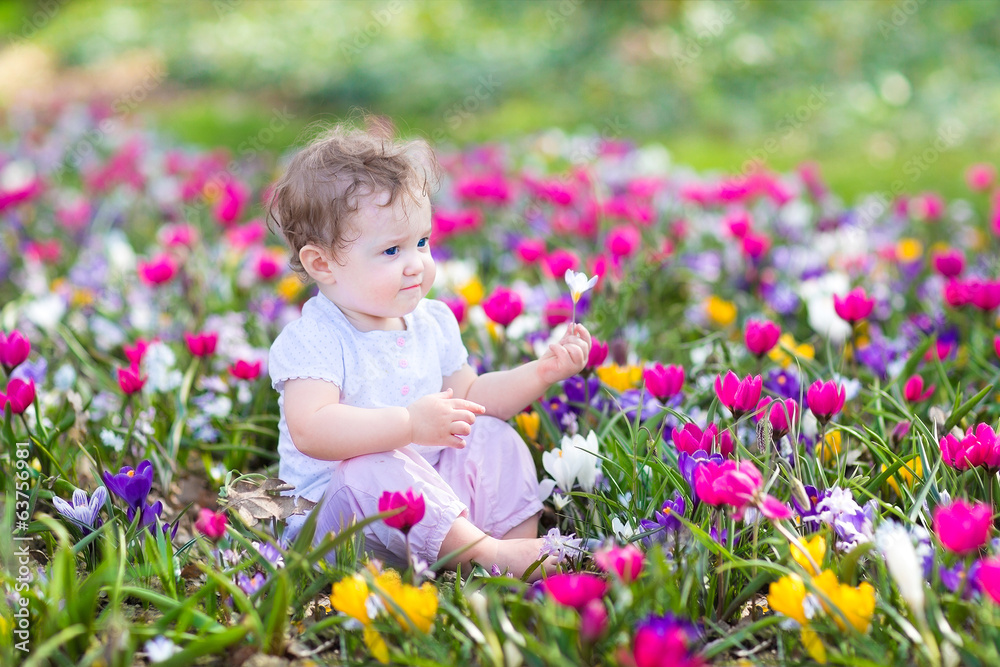 Cute curly little baby sitting between beautiful spring flowers Cute curly little baby sitting between beautiful spring flowers