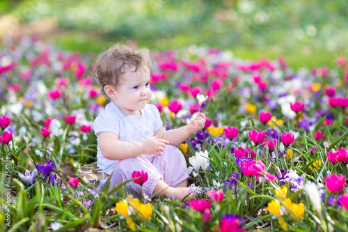 Cute curly little baby sitting between beautiful spring flowers
