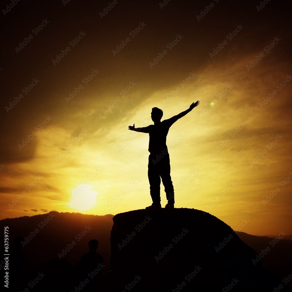 man silhouette with her hand raised in the sunset man silhouette with her hand raised in the sunset