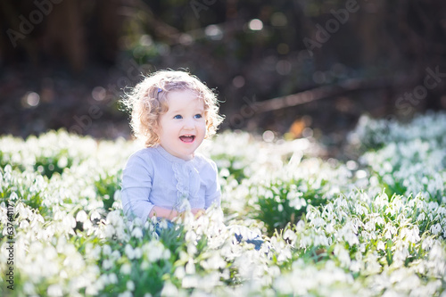 Adorable curly toddler girl playing with first spring flowers