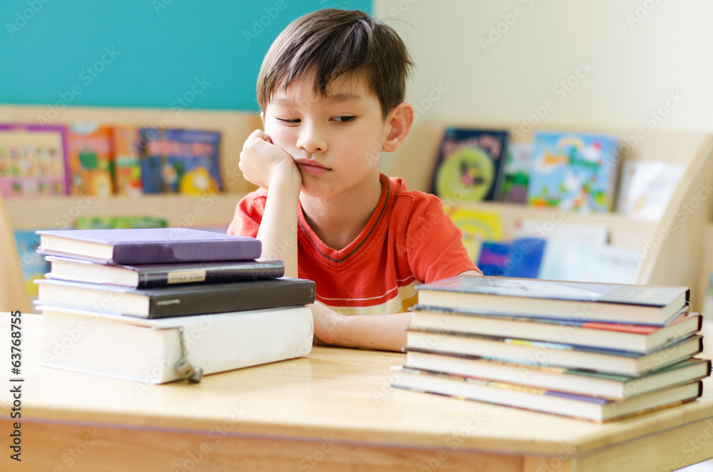 Little boy reading book on table at home with boring face Little boy reading book on table at home with boring face